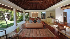 Uma sala de estar ampla com teto alto, um sofá com almofadas, uma mesa de jantar com cadeiras e vista para o exterior.