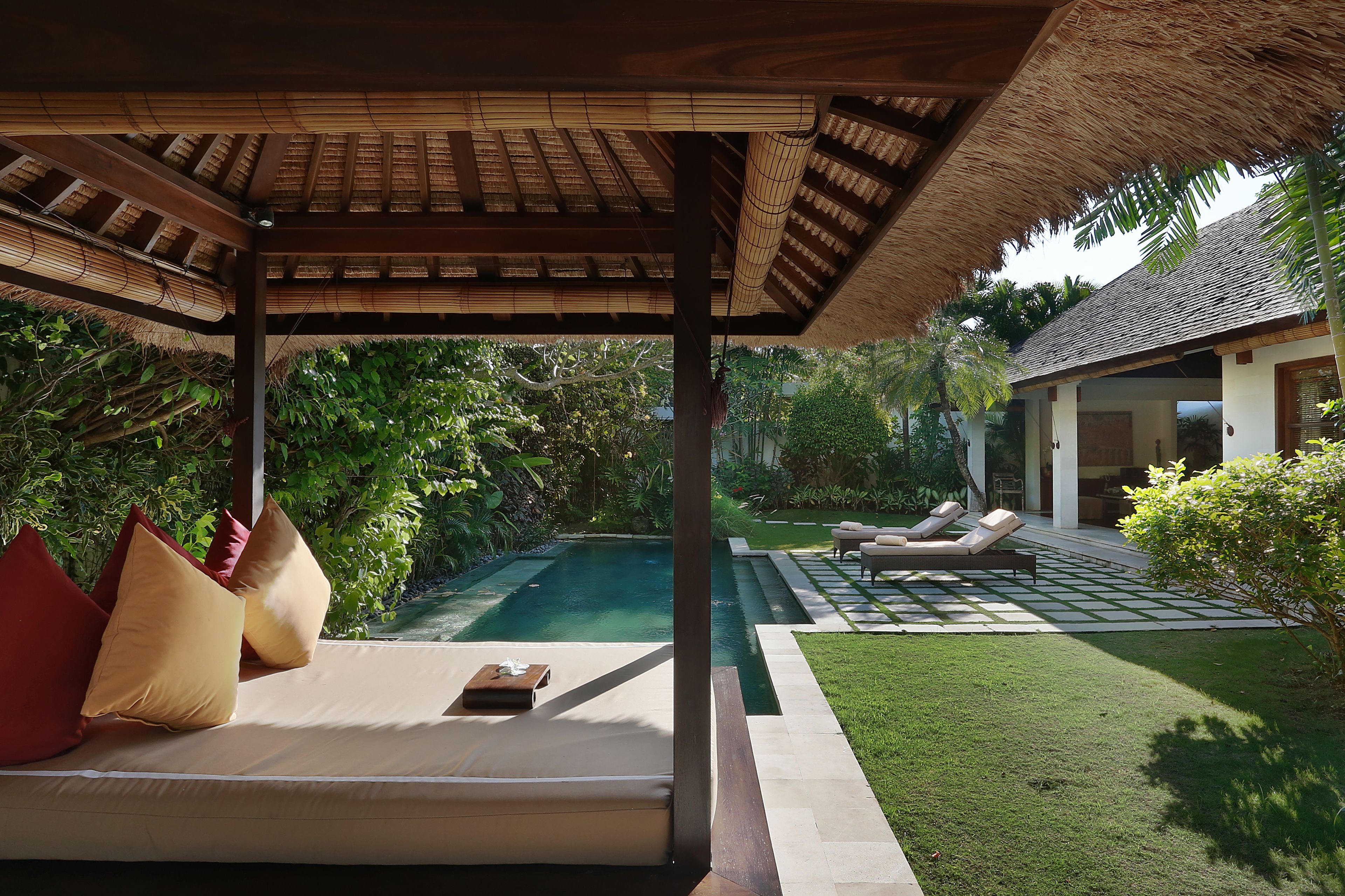 A covered outdoor seating area with a pool, lounge chairs, and a well-maintained garden.