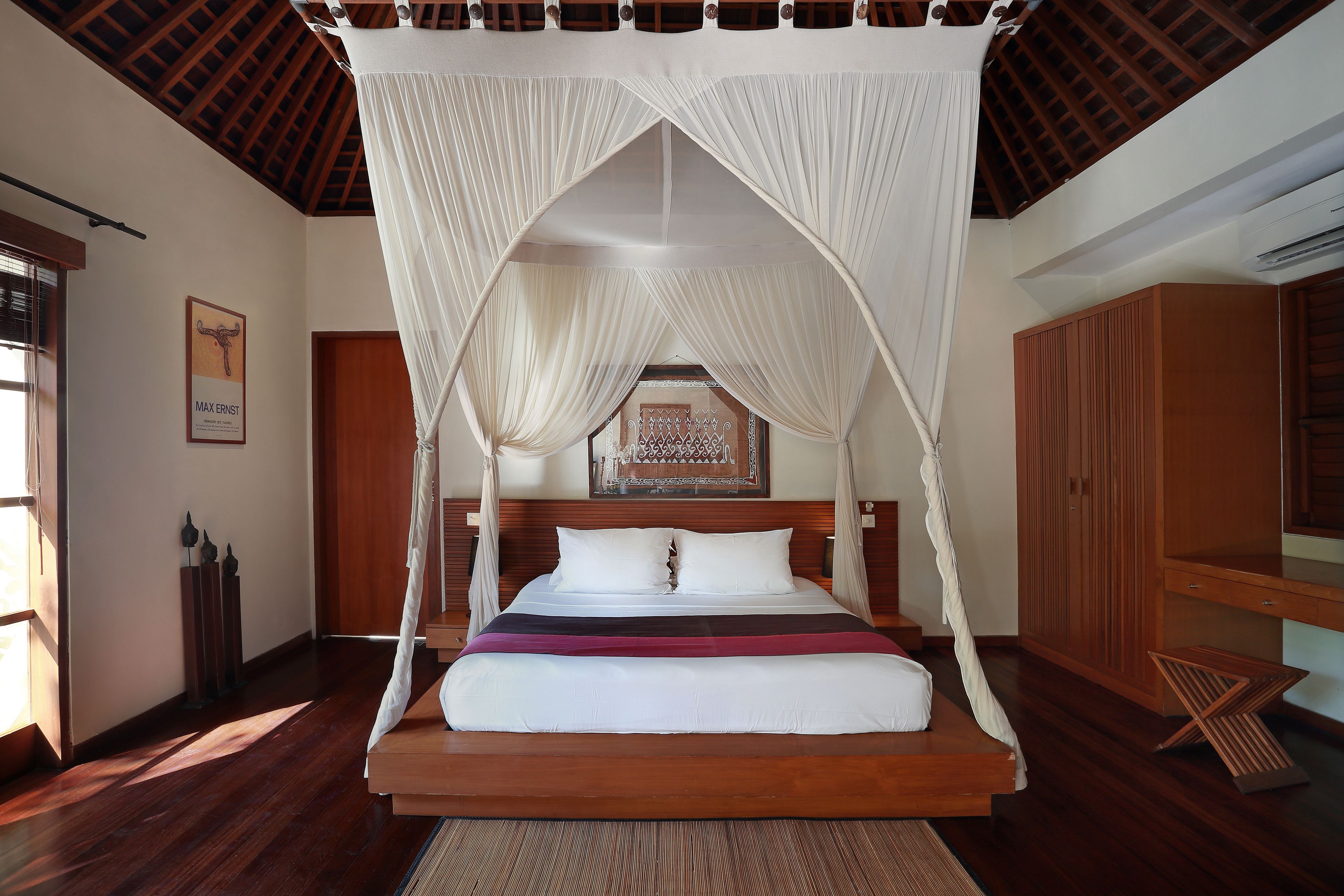 A bed with a canopy, wooden flooring, and a framed picture on the wall.