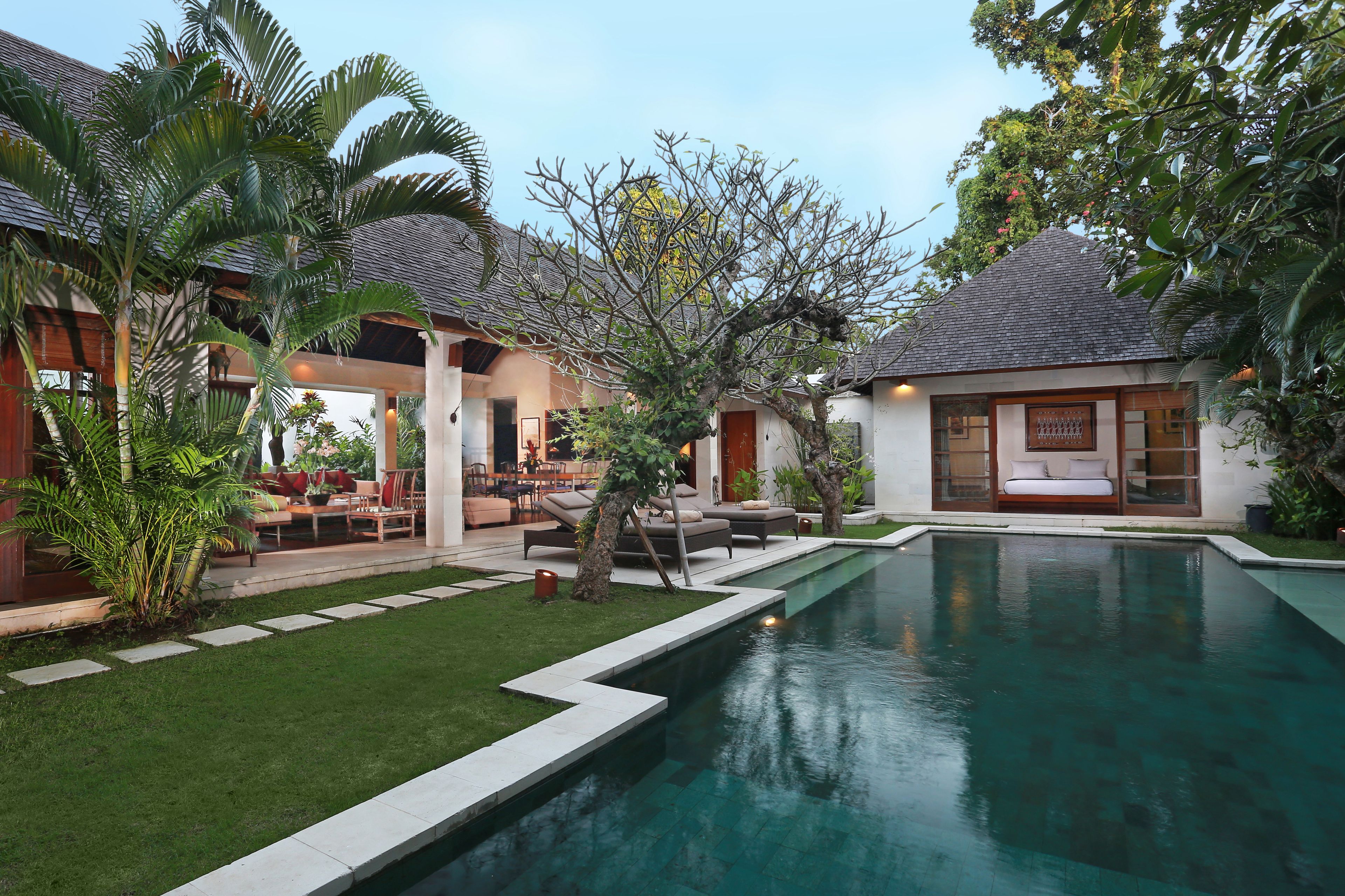 A poolside area with a clear pool, outdoor seating, and lush greenery.
