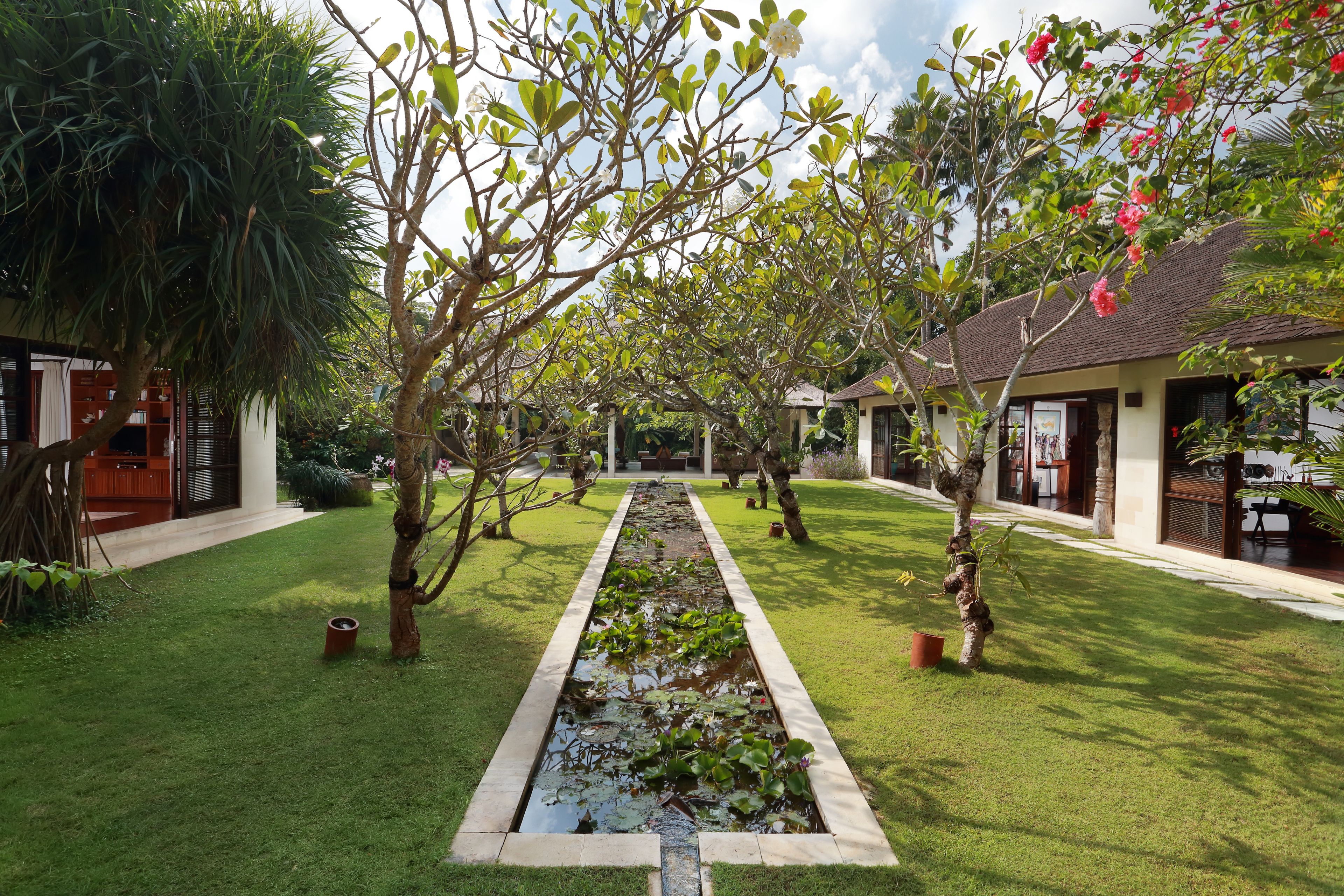 Un jardín con fuente de agua, árboles y un sendero que lleva a un edificio.