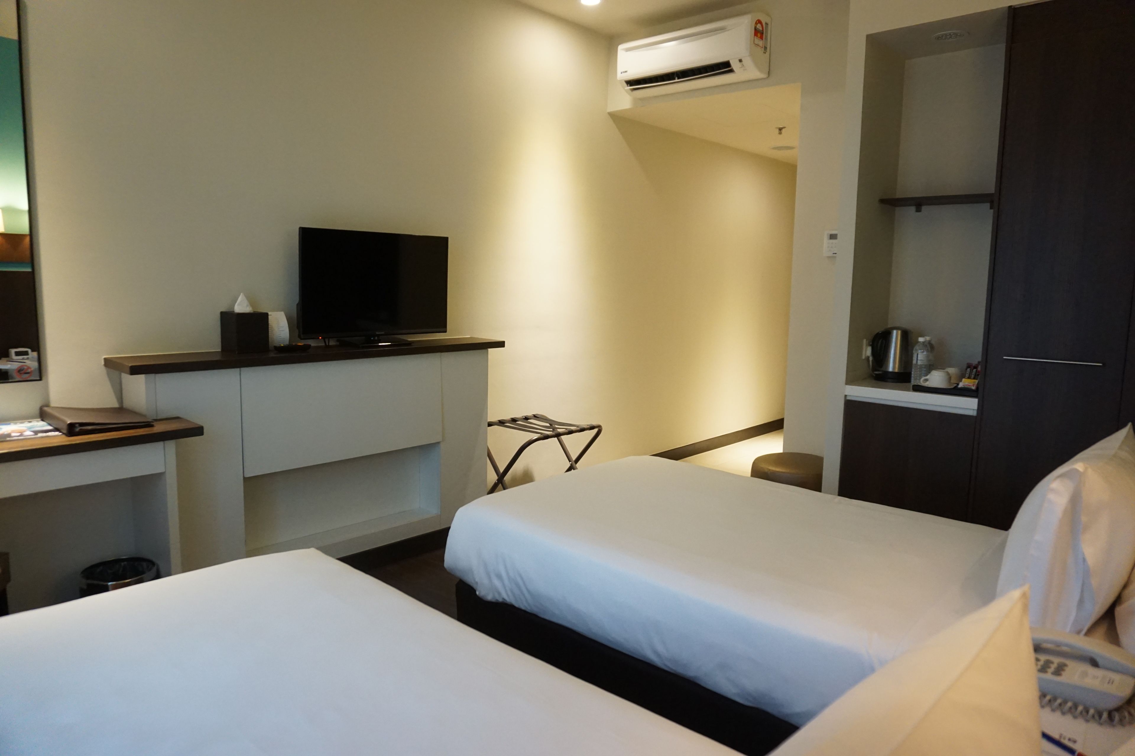 Habitación de hotel con dos camas, un televisor de pantalla plana sobre un soporte, un escritorio con una computadora portátil y una caja de pañuelos, y un armario.