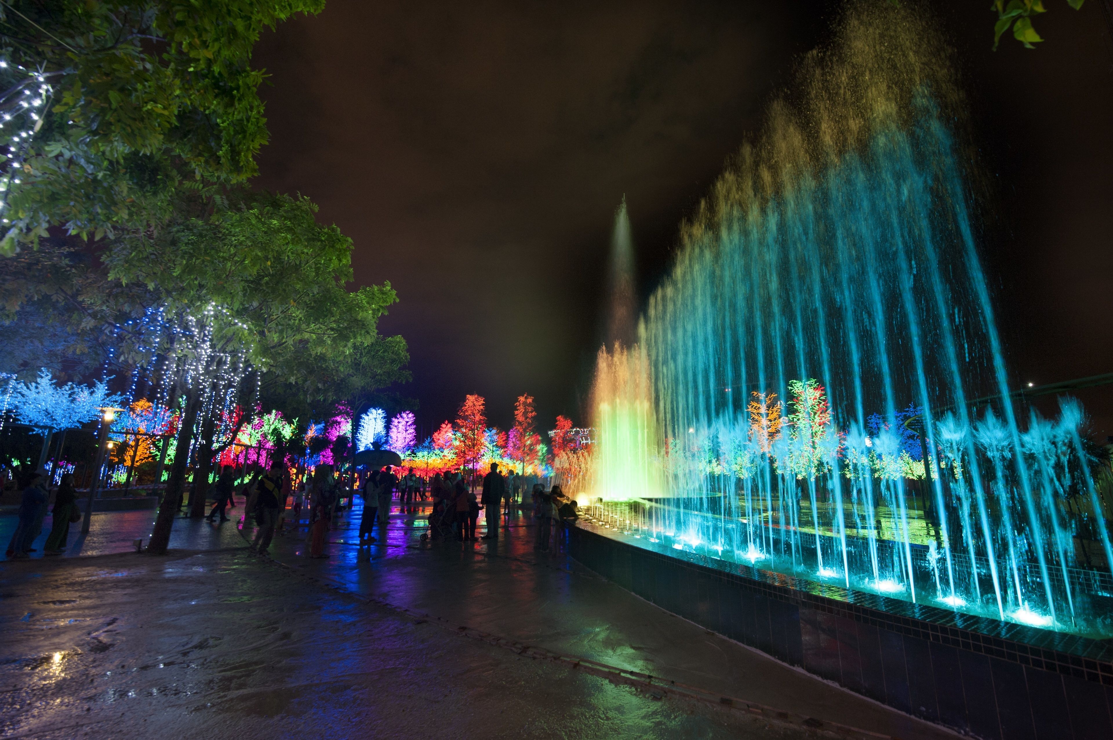 A nighttime outdoor area with a fountain and illuminated trees.