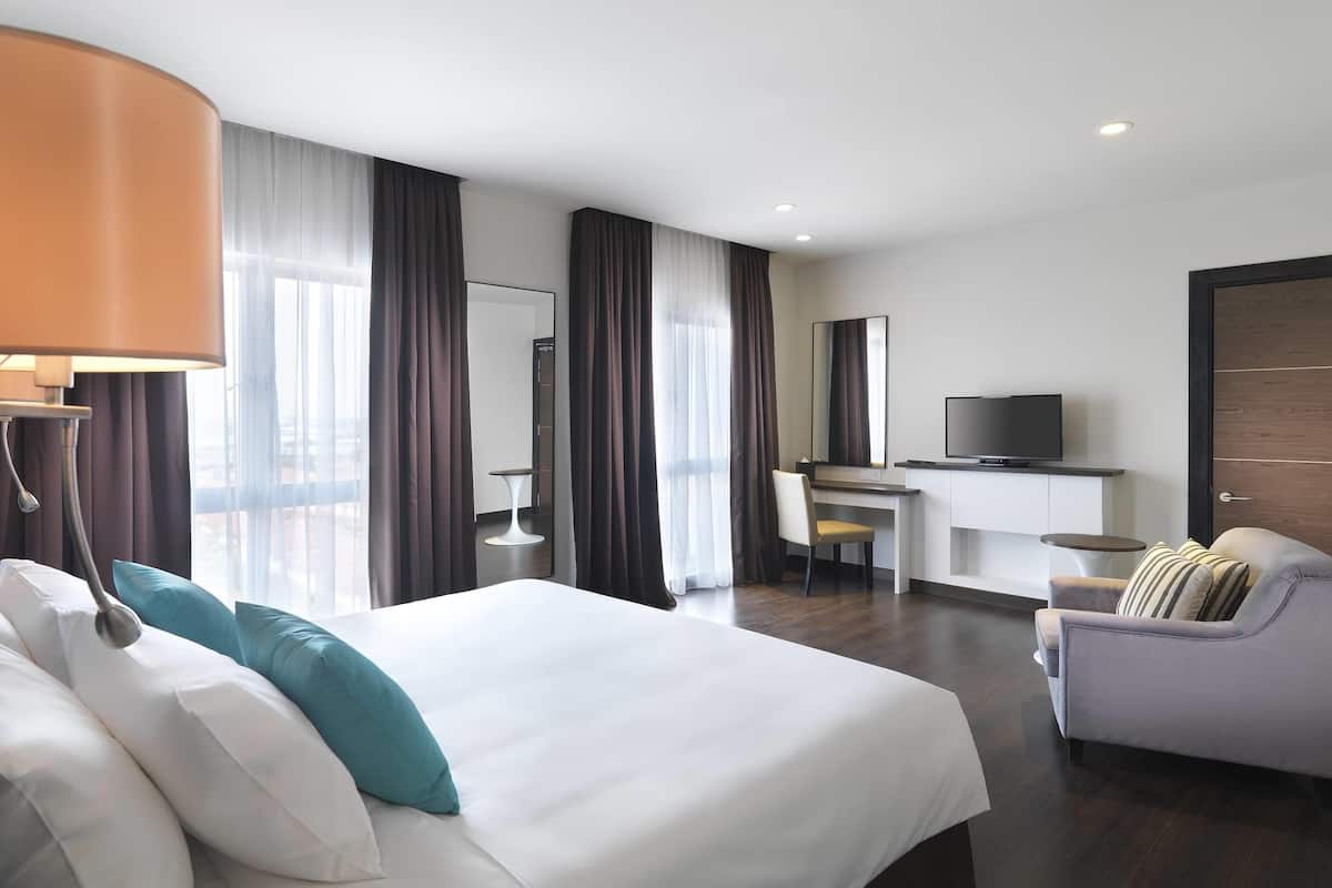 A hotel room with a large bed, a desk with a chair, a television, and a sofa.