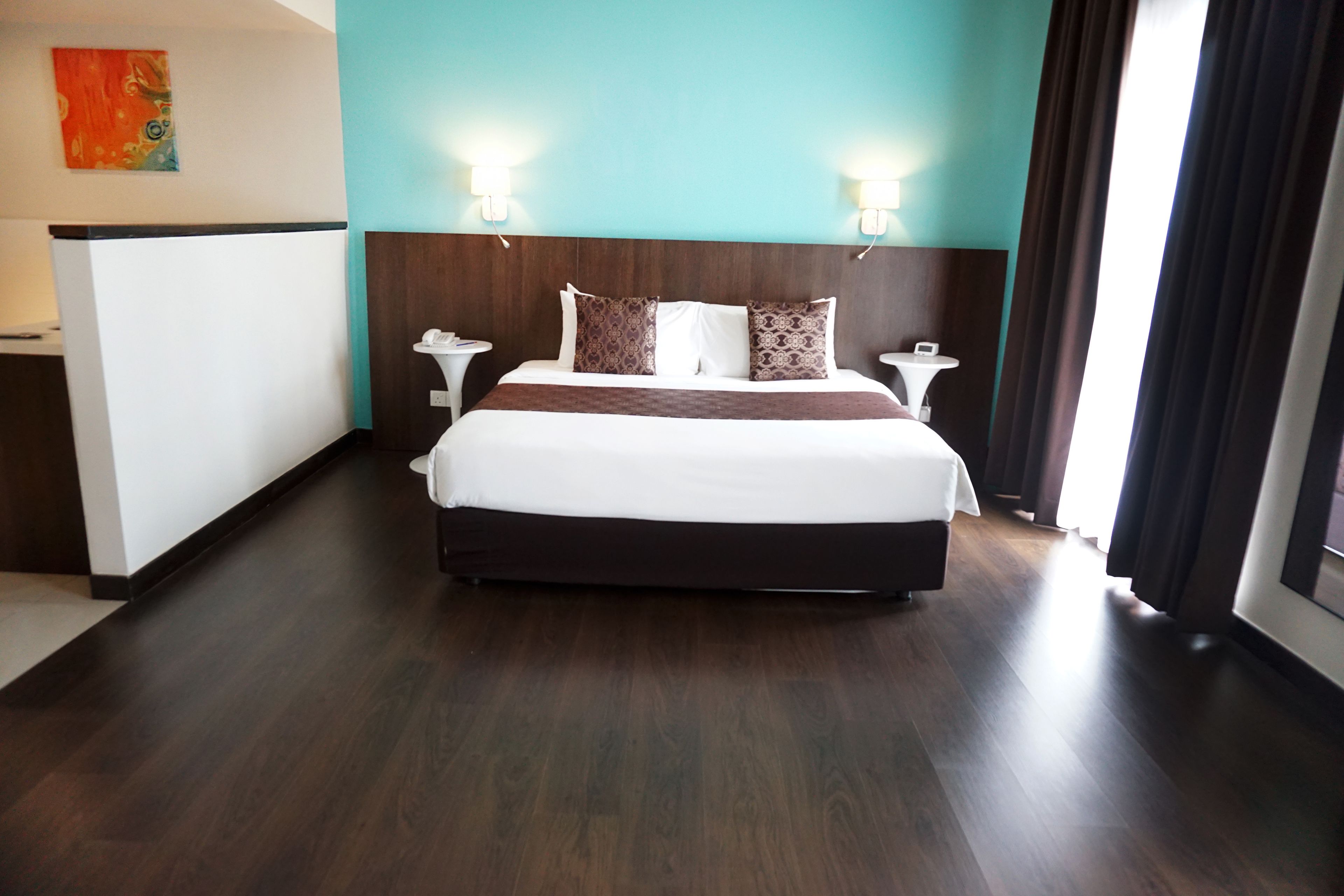 A hotel room with a large bed, two bedside tables, a nightstand, a wall-mounted TV, and a window with curtains.