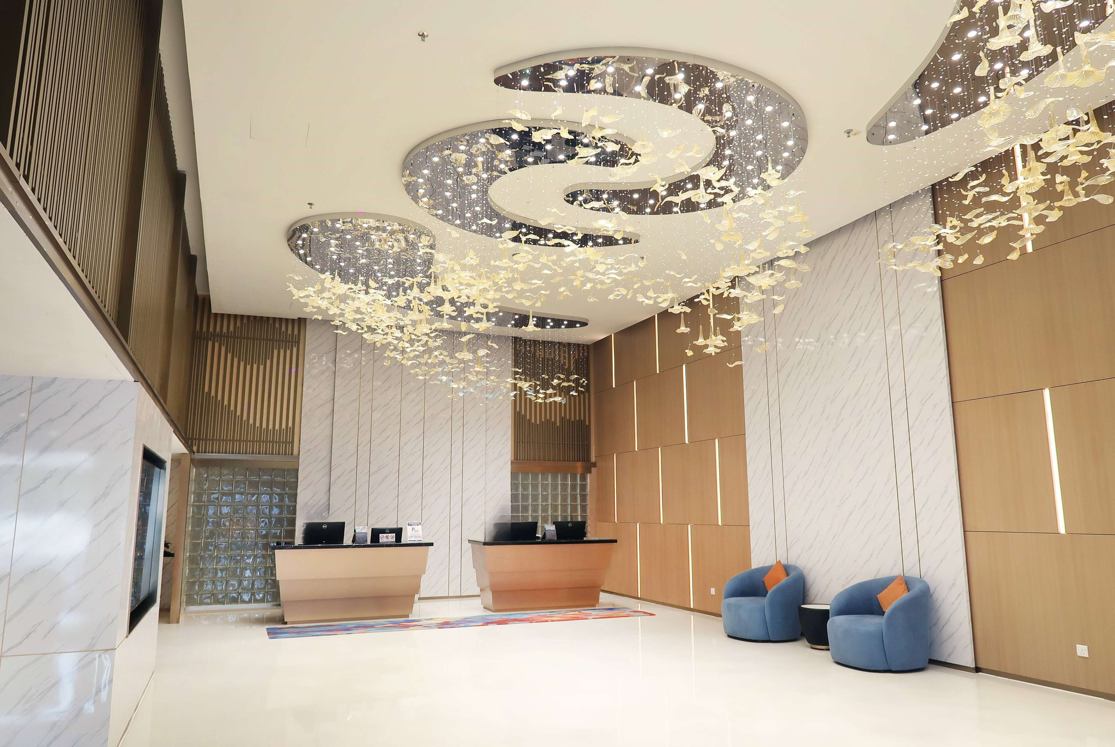 A modern reception area with a marble reception desk, a blue seating area, and a decorative ceiling with hanging elements.