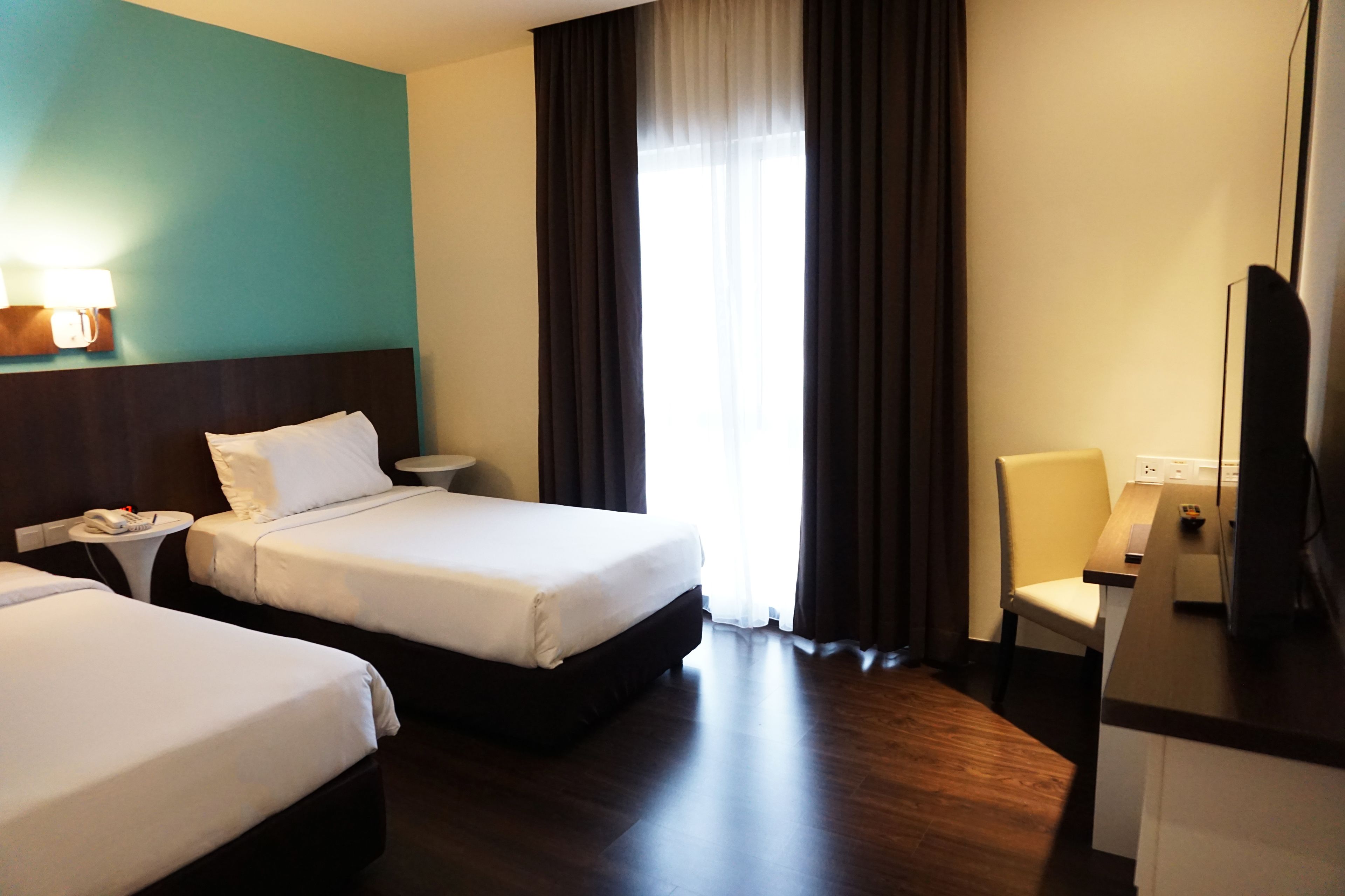A hotel room with two beds, a desk, a chair, a TV, and a window with curtains.