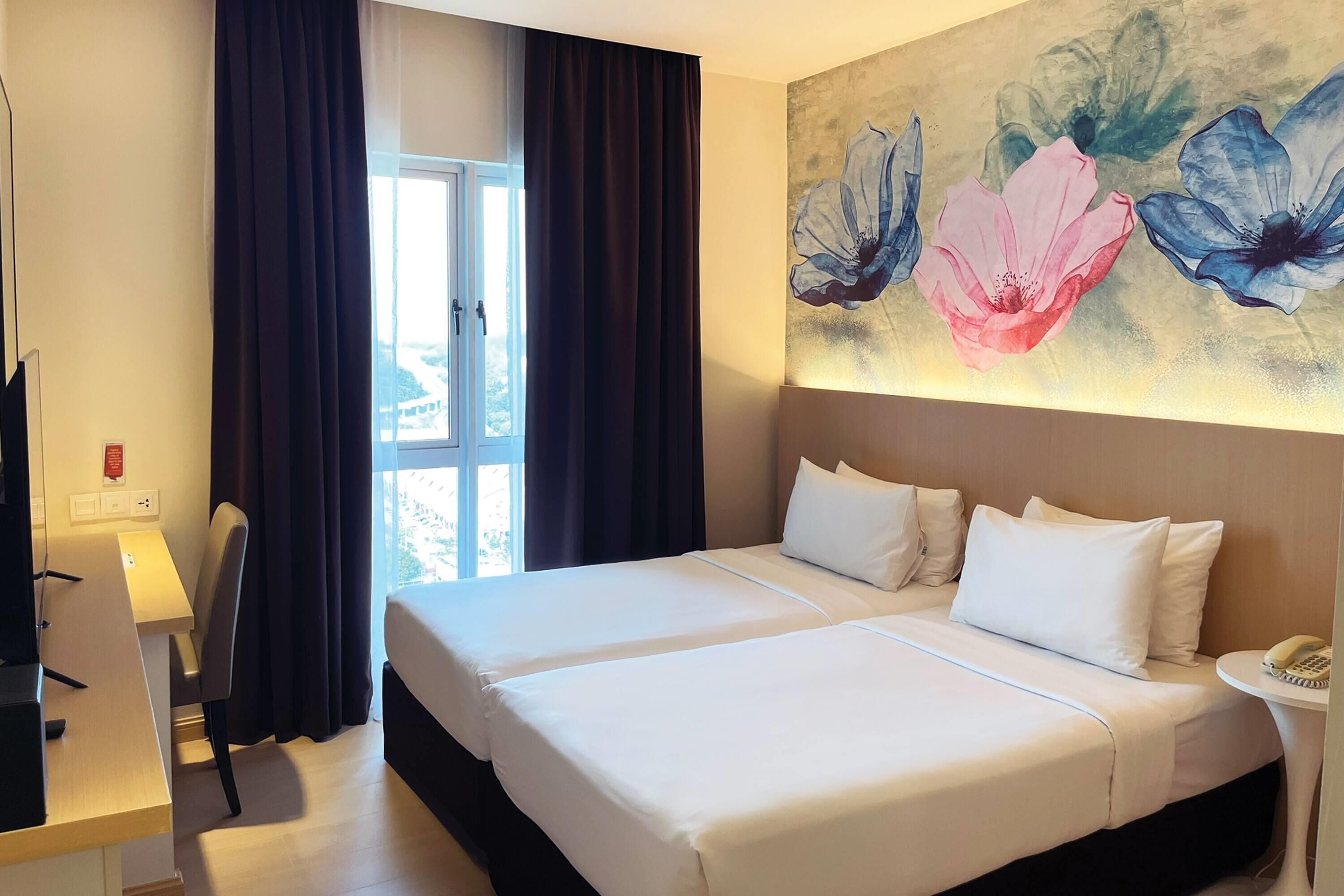 Una habitación de hotel con una cama, un escritorio y un cuadro de flores en la pared.