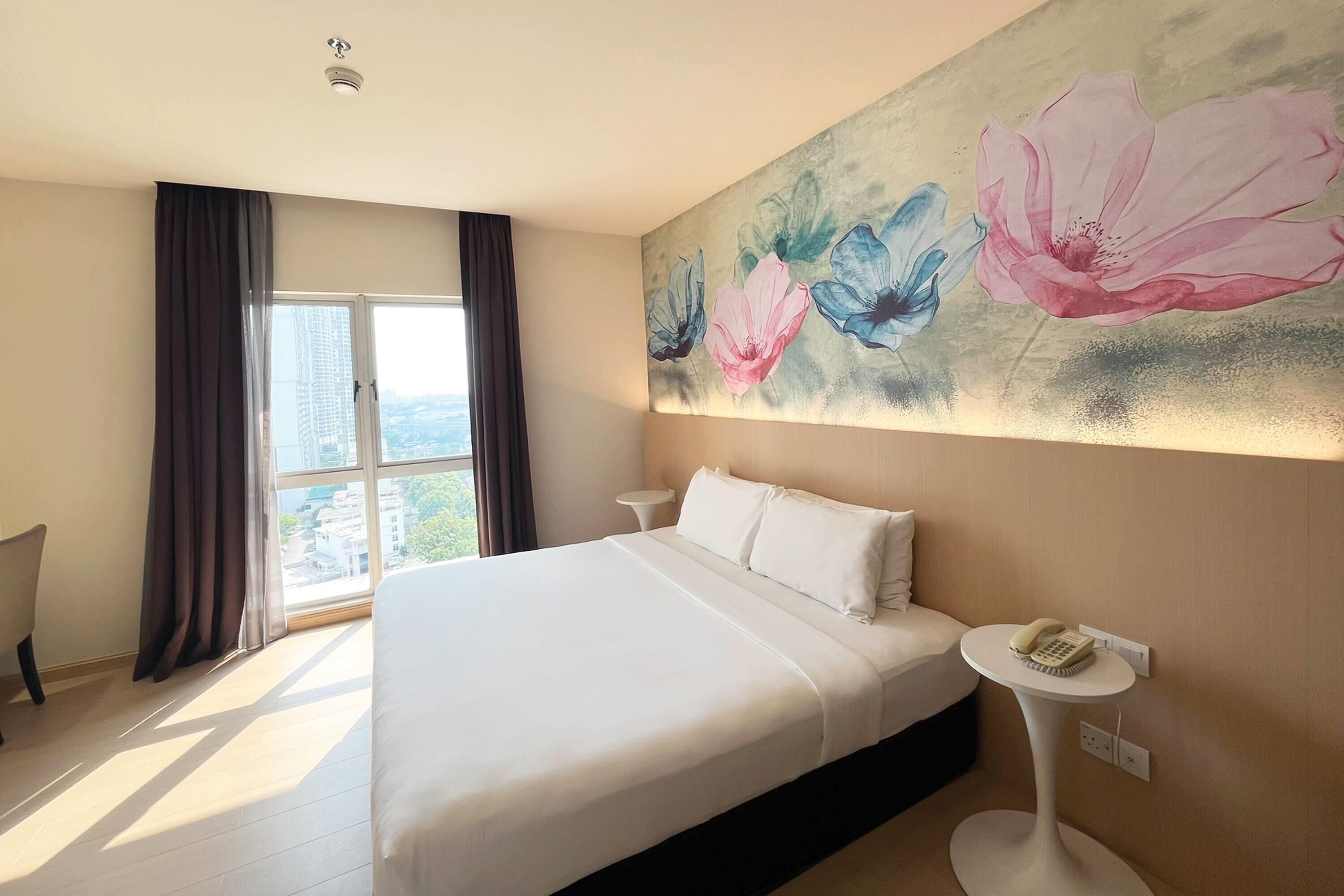 Ein Hotelzimmer mit einem großen Bett, einem Nachttisch mit Telefon und einem Fenster mit Vorhängen.