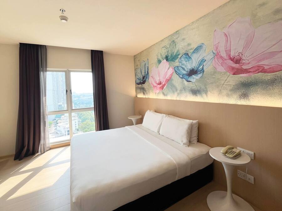Ein Hotelzimmer mit einem großen Bett, einem Nachttisch mit Telefon und einem Fenster mit Vorhängen.