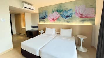 Une chambre d’hôtel avec un lit double, une table de chevet, un climatiseur fixé au mur et un tableau représentant des fleurs au-dessus du lit.