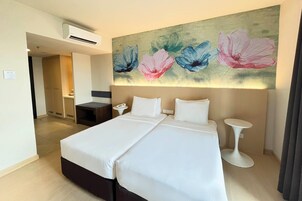 Une chambre d’hôtel avec un lit double, une table de chevet, un climatiseur fixé au mur et un tableau représentant des fleurs au-dessus du lit.