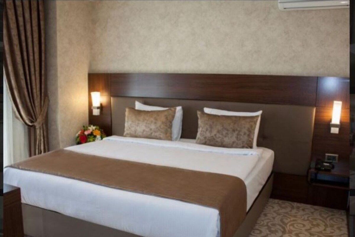 A hotel room with a large bed, two bedside lamps, a nightstand, and a floral arrangement.