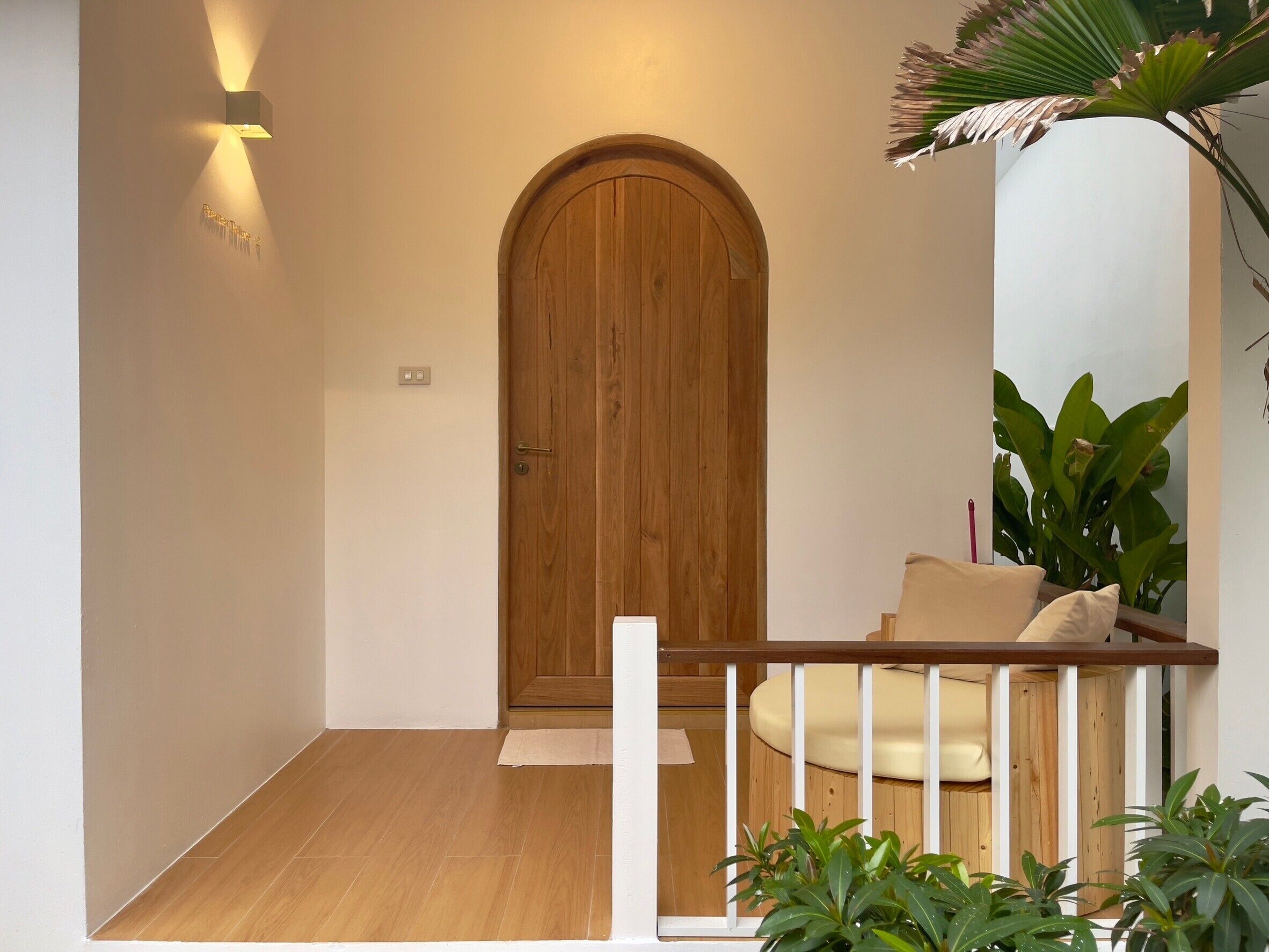 A wooden door with a white frame, a small step leading up to it, and a white railing with a beige cushion.