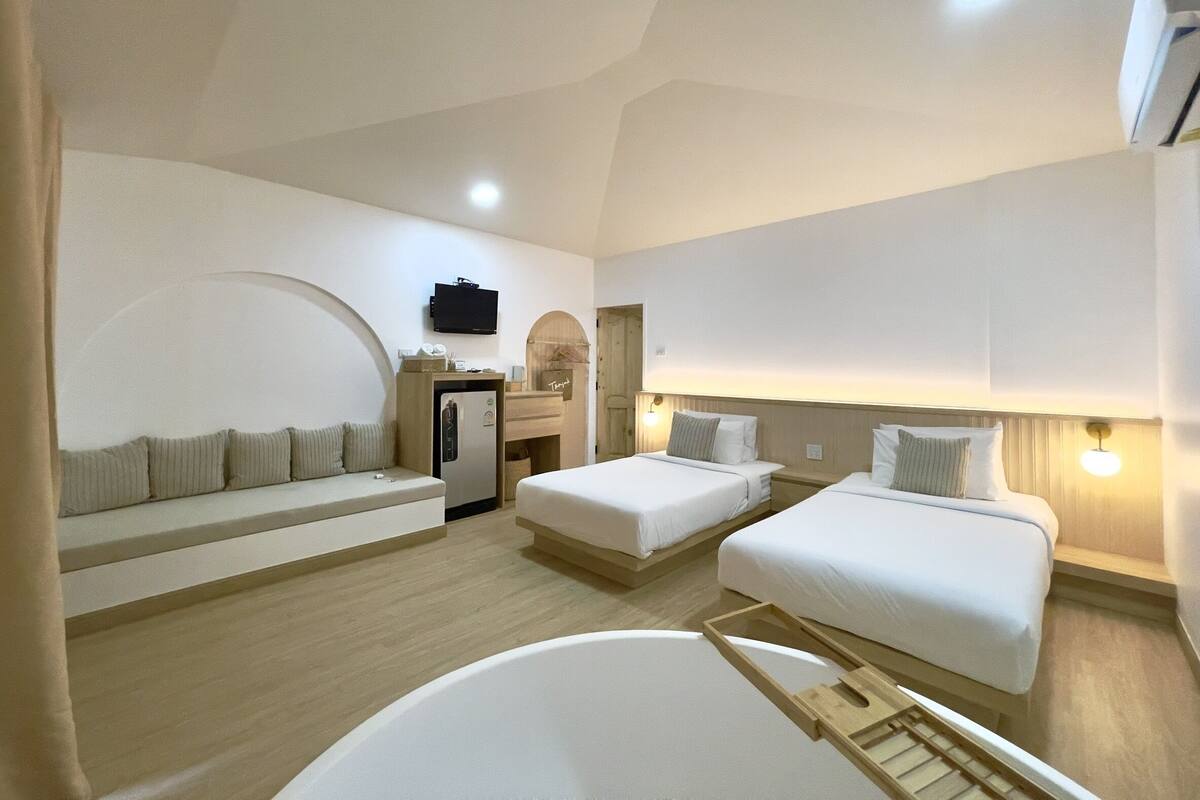 Quarto de hotel com duas camas, um sofá, uma TV, frigobar e iluminação no teto.