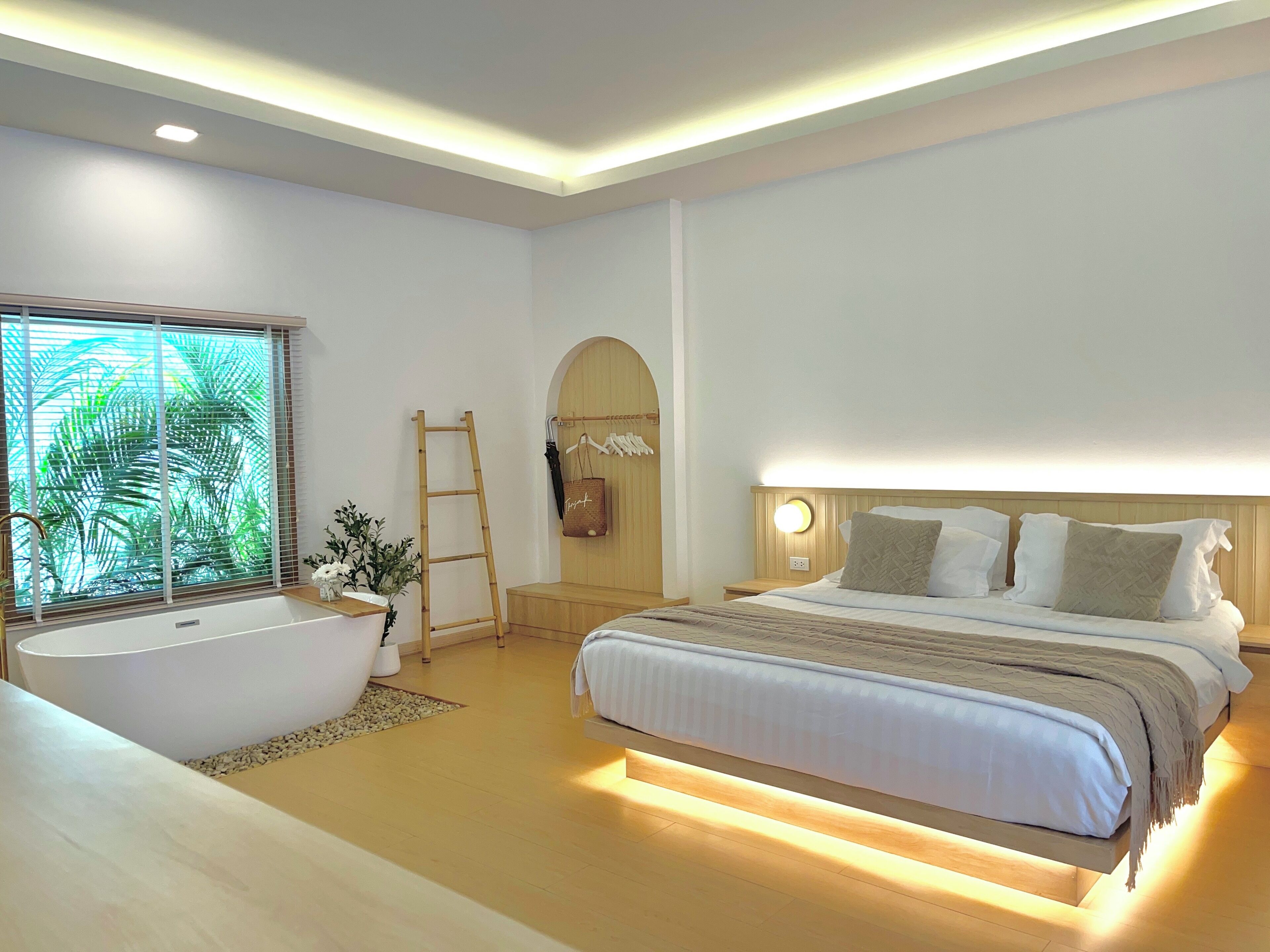 A modern bedroom with a large bed, a bathtub, and a wooden ladder.