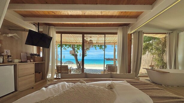 Un dormitorio con una cama grande, televisión, vista a la playa y techo de madera.