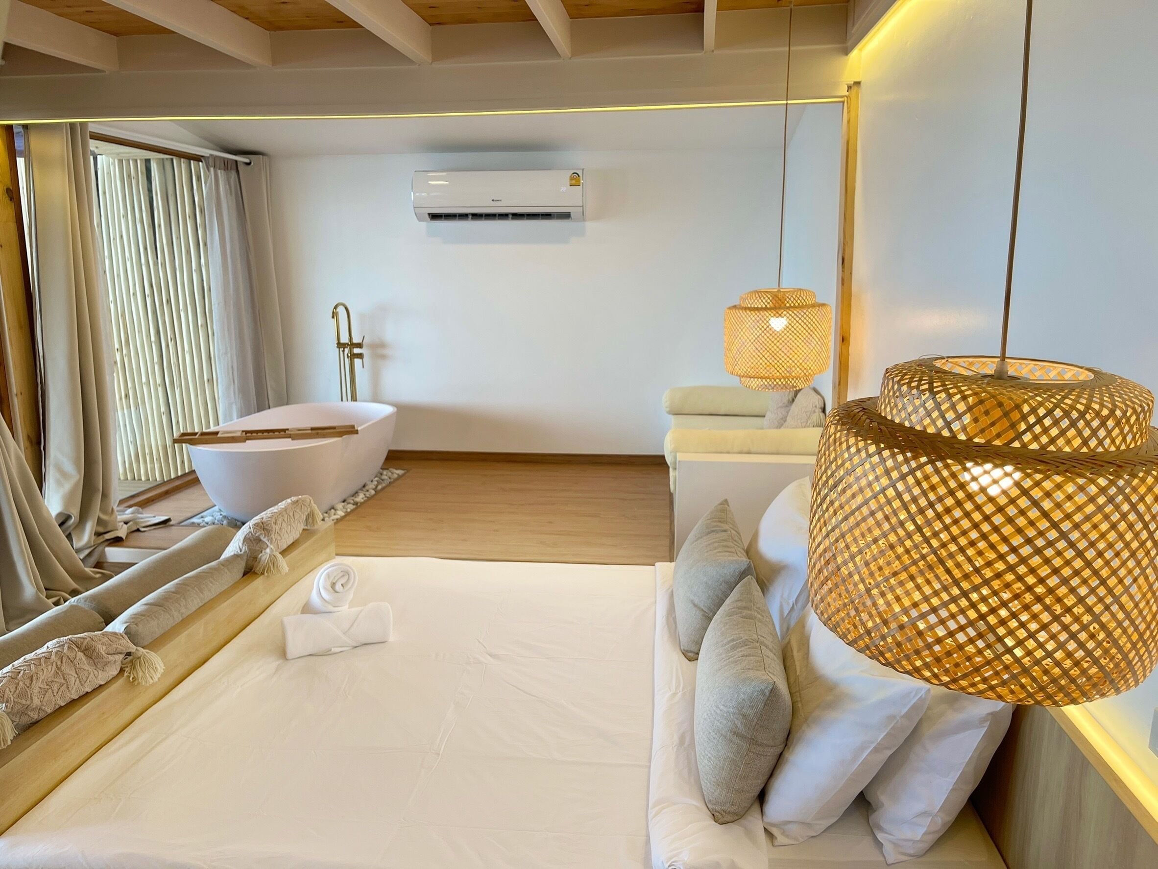 Ein modernes Schlafzimmer mit einem großen Bett, einer Badewanne, einer hängenden Rattanlampe und einer Klimaanlage an der Wand.
