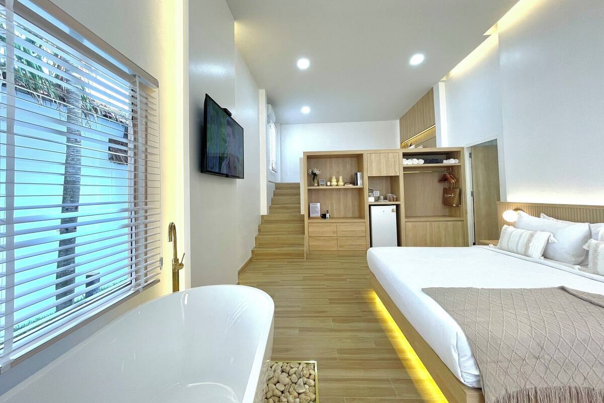 Quarto de hotel moderno com uma cama grande, uma cama menor, uma toucador com espelho, televisão e escada que leva a um andar superior.