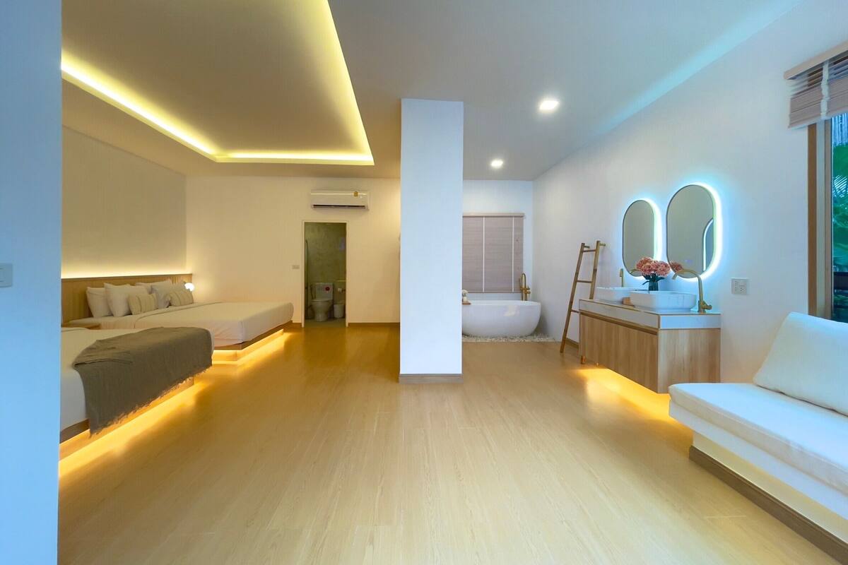 Quarto de hotel moderno com uma cama grande, área de estar, banheiro com banheira e toucador com espelhos.