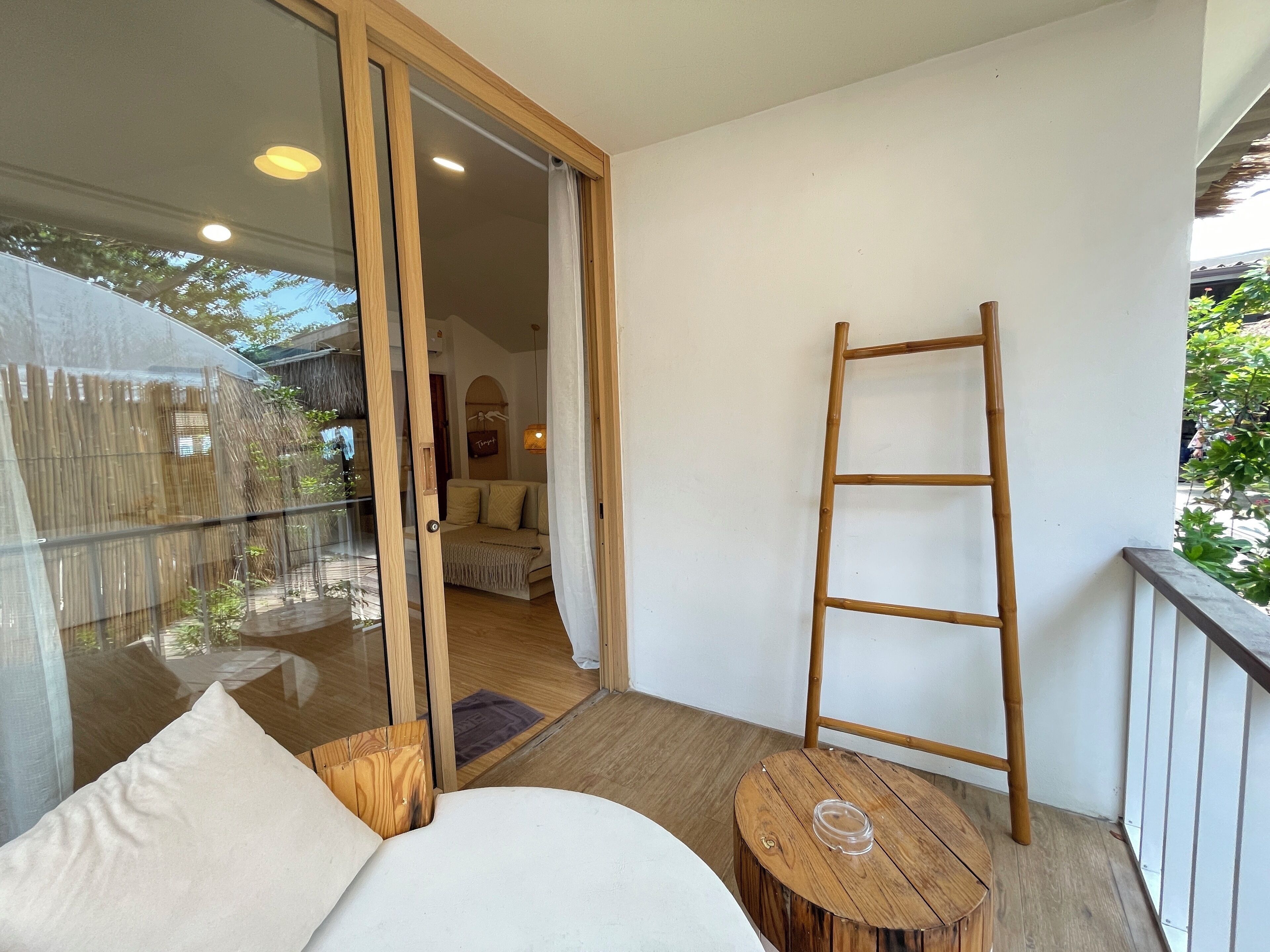 A balcony with a wooden ladder, a round wooden table, and a sofa with cushions.