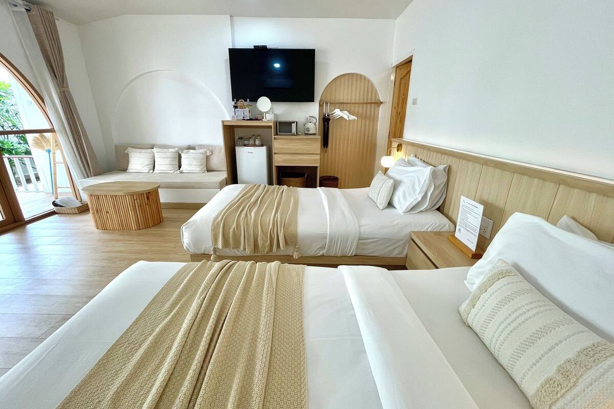 Quarto de hotel com duas camas, televisão, escrivaninha e vista para o exterior.
