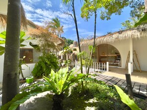 A tropical resort with thatched-roof structures, a central garden area, and a large arched window.