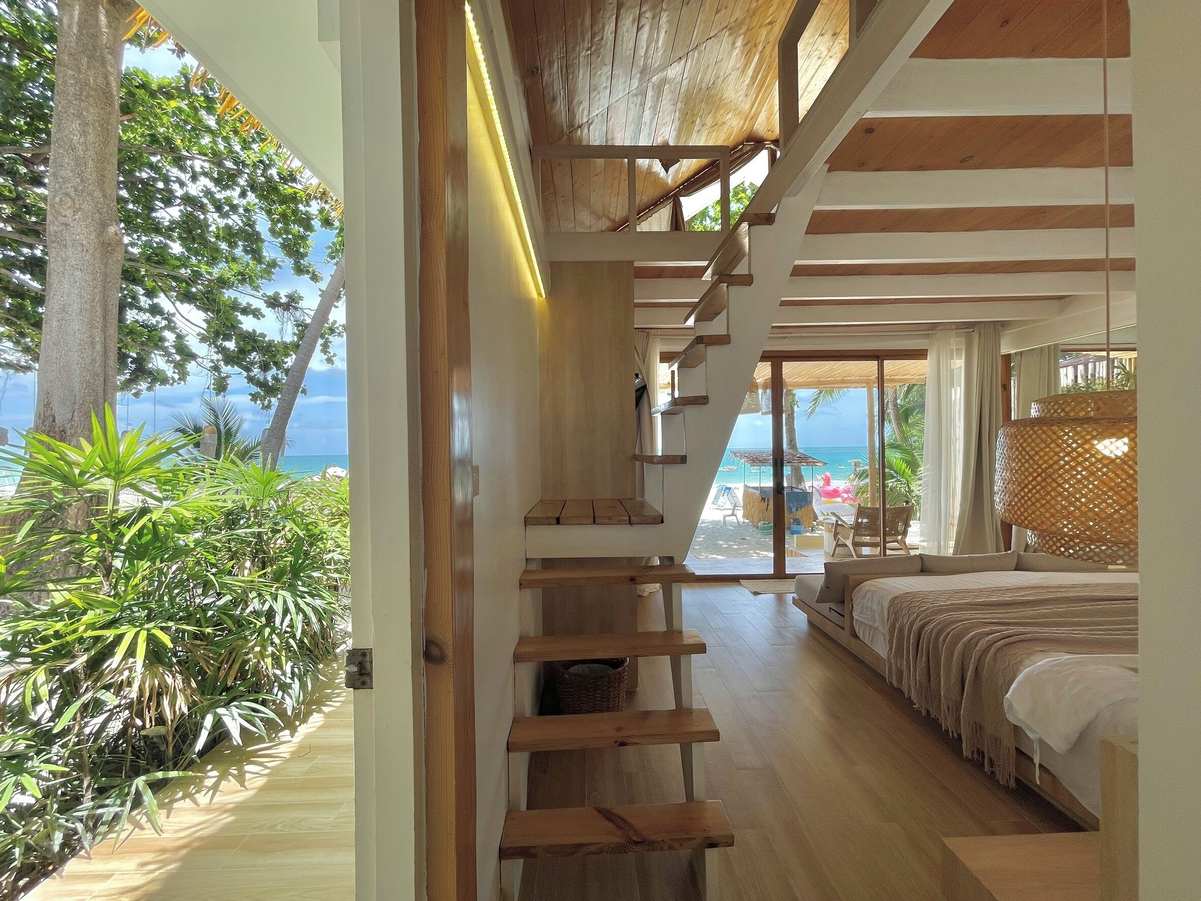 A bedroom with a wooden staircase leading to a balcony overlooking the sea.