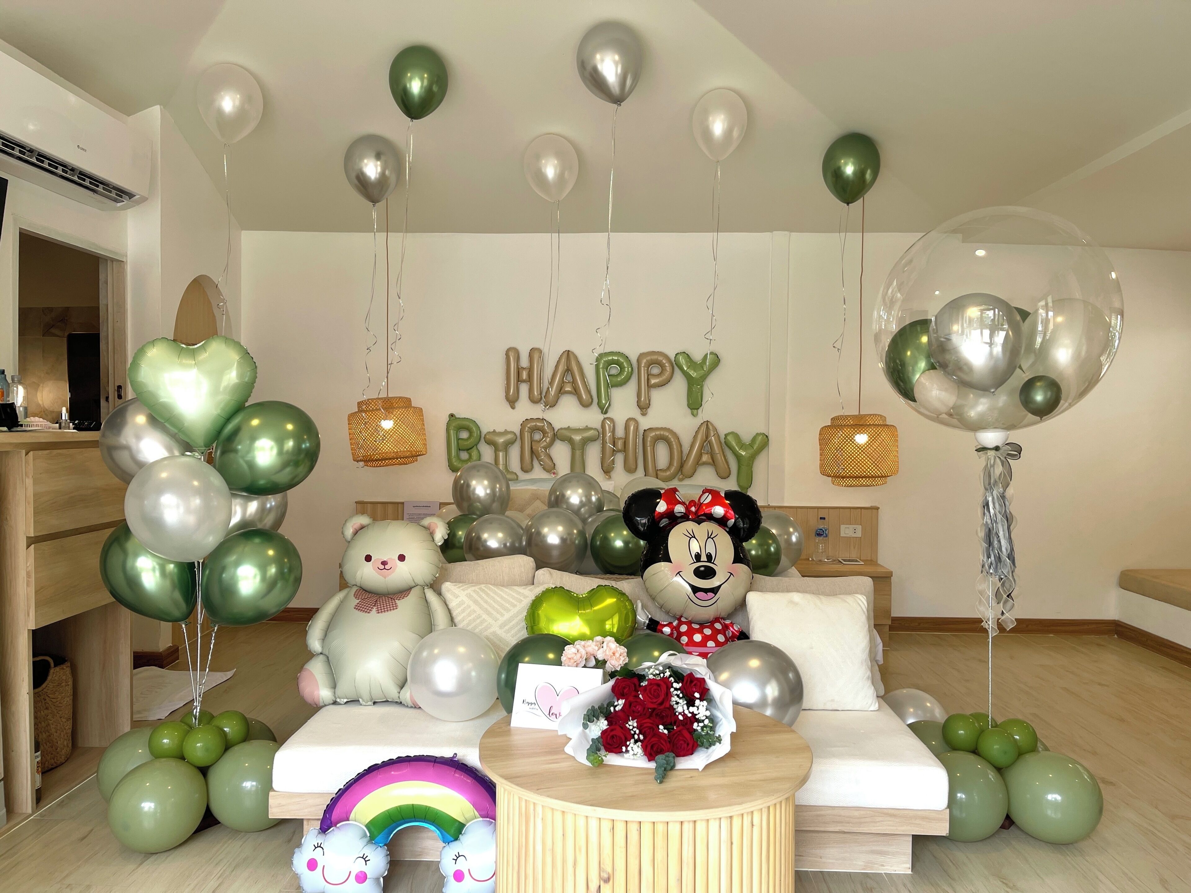 Een kamer met een bed, een ronde houten tafel, ballonnen en een 'HAPPY BIRTHDAY' bord.