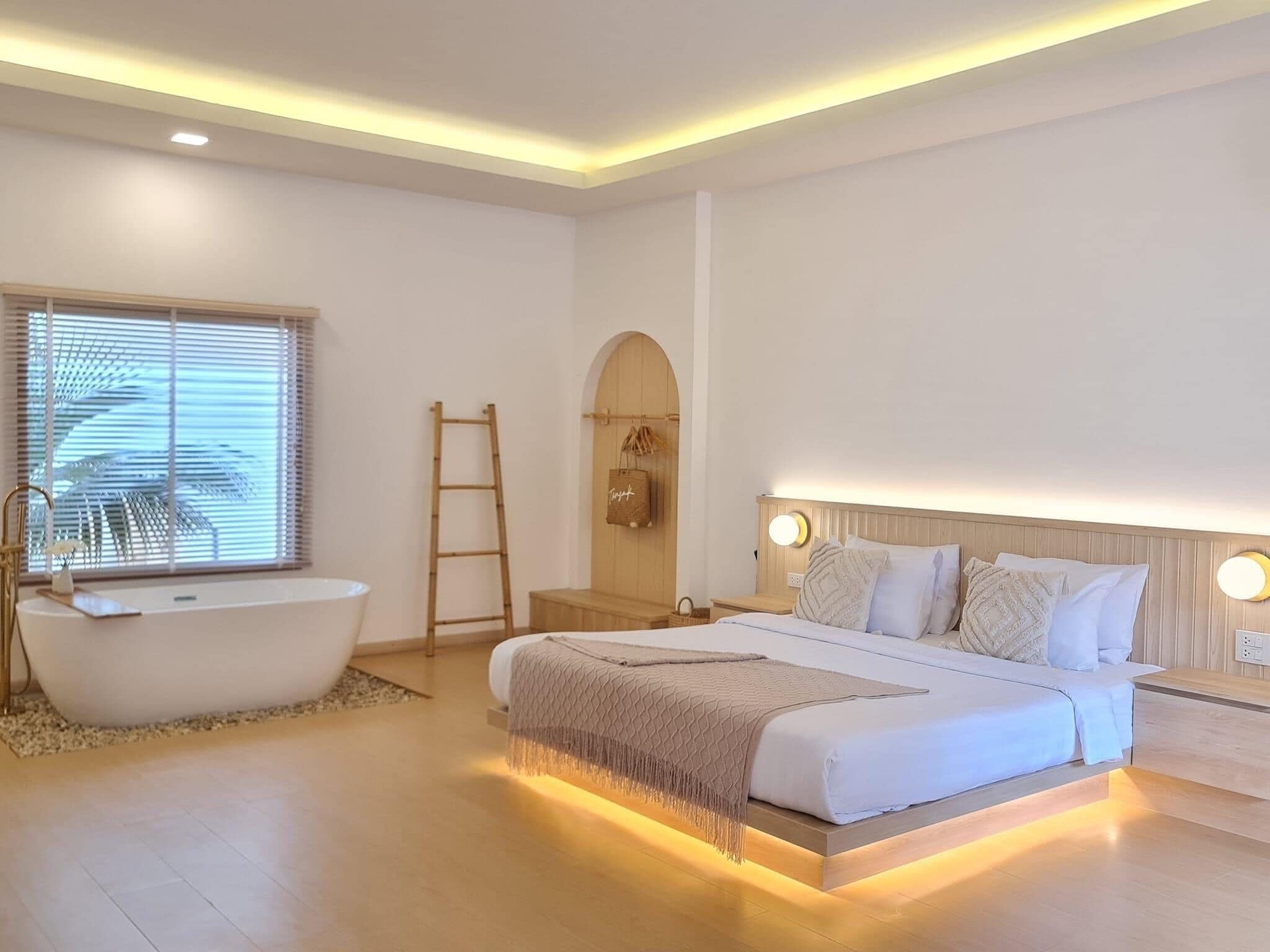 A modern bedroom with a large bed, a built-in bathtub, and a wooden ladder.