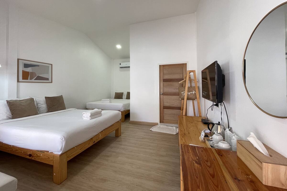 Quarto de hotel com duas camas de solteiro, cômoda de madeira, espelho, televisão e uma pequena mesa com caixa de lenços.