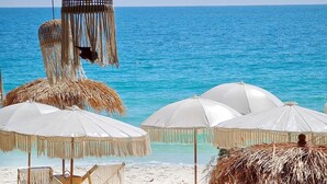 Una playa con sombrillas de techo de paja y sillones de descanso, vista despejada del océano y arena dorada.