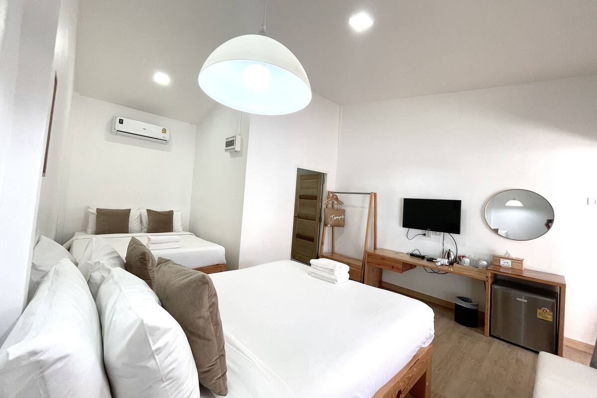 Quarto de hotel com duas camas, uma escrivaninha com televisão, um espelho e um frigorífico pequeno.