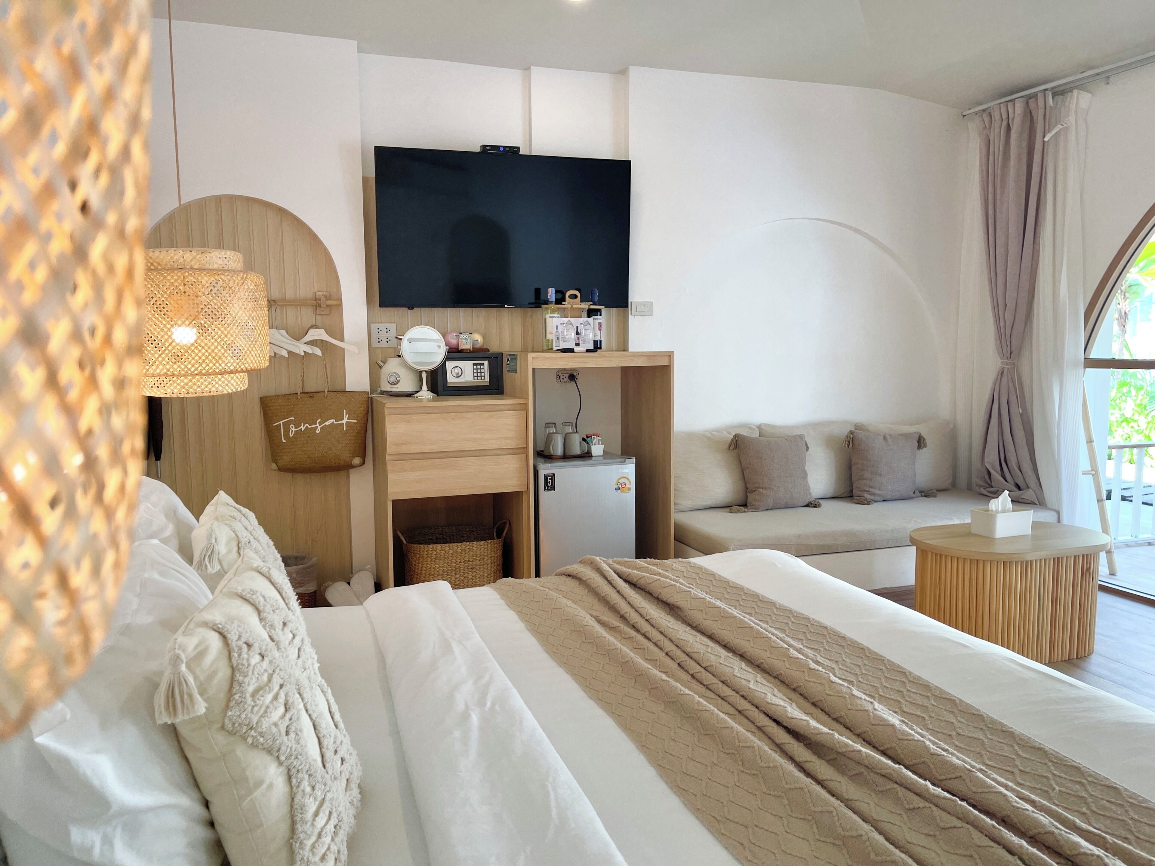 Una habitación de hotel con cama, televisión, escritorio, refrigerador pequeño, sofá y ventana con cortinas.