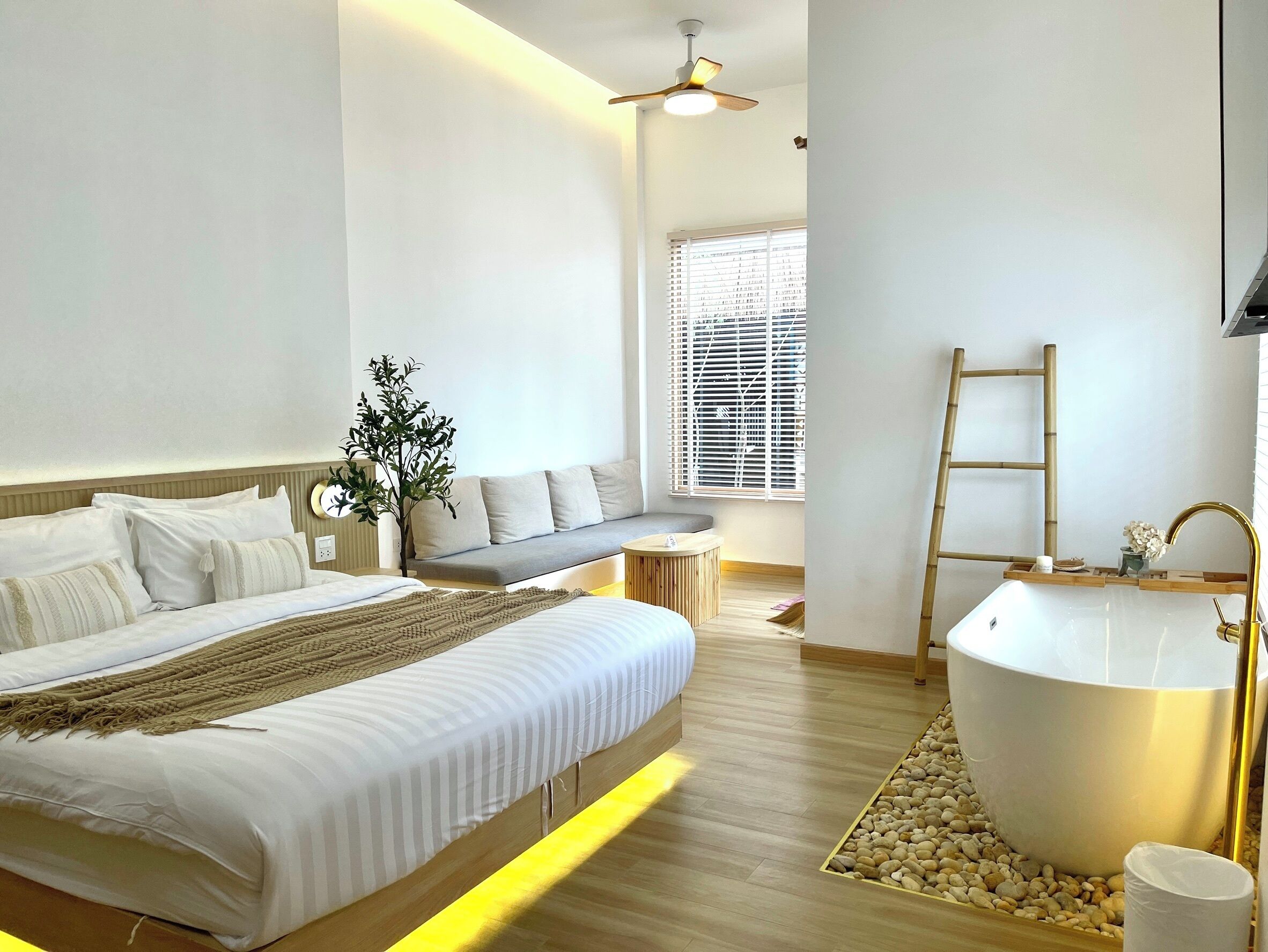 Una habitación de hotel moderna con una cama grande, una zona de estar, una bañera y una ventana con persianas.