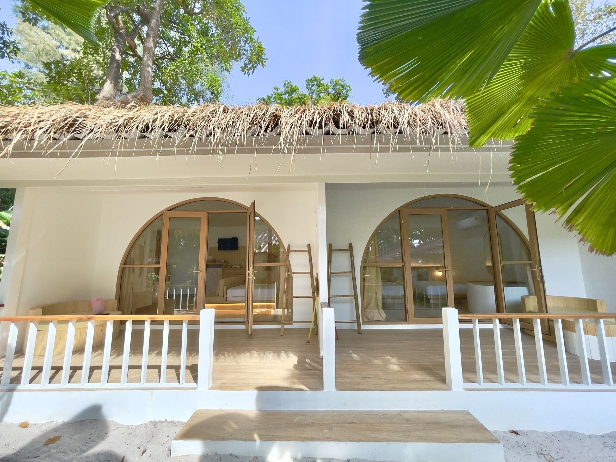 A two-story building with a thatched roof, large arched windows, and a wooden deck with a white railing.