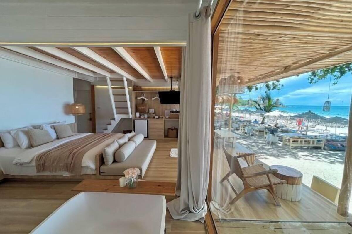 Quarto com cama, sofá, escrivaninha e vista para a praia.