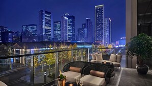 A rooftop lounge with a city view, featuring a glass table with champagne and glasses, cushioned seating, and a potted plant. - Niccolo Chengdu (Chengdu)