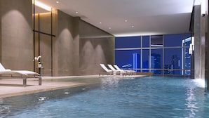 An indoor swimming pool with lounge chairs and a city view at night. - Niccolo Chengdu (Chengdu)