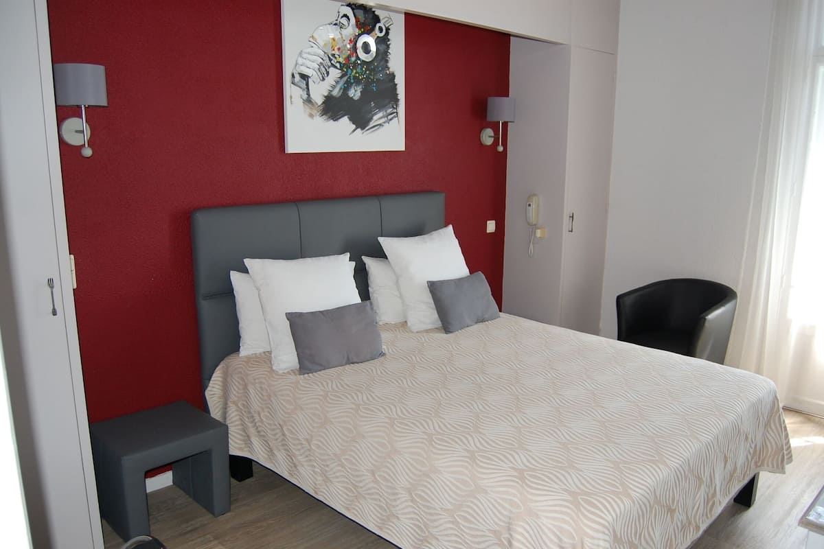 A bedroom with a bed, bedside lamps, a small stool, and a painting on the wall.