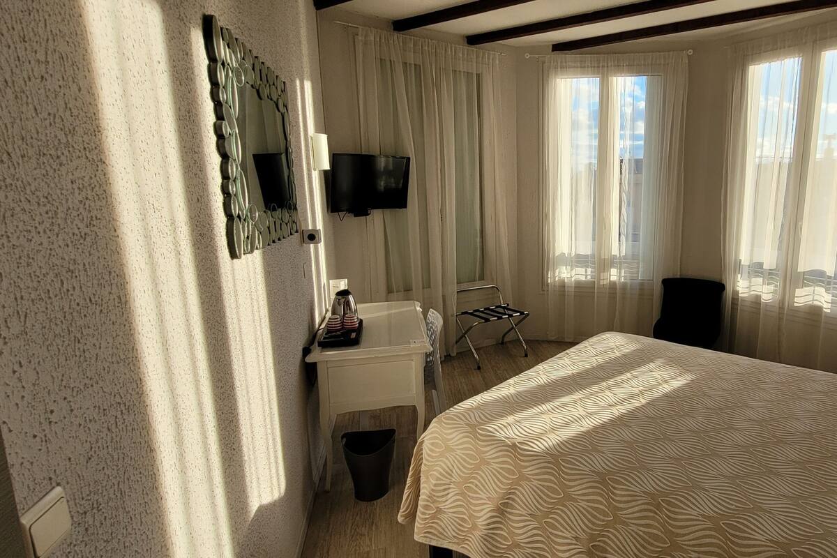 A hotel room with a bed, a desk, a chair, a TV, and a window with curtains.