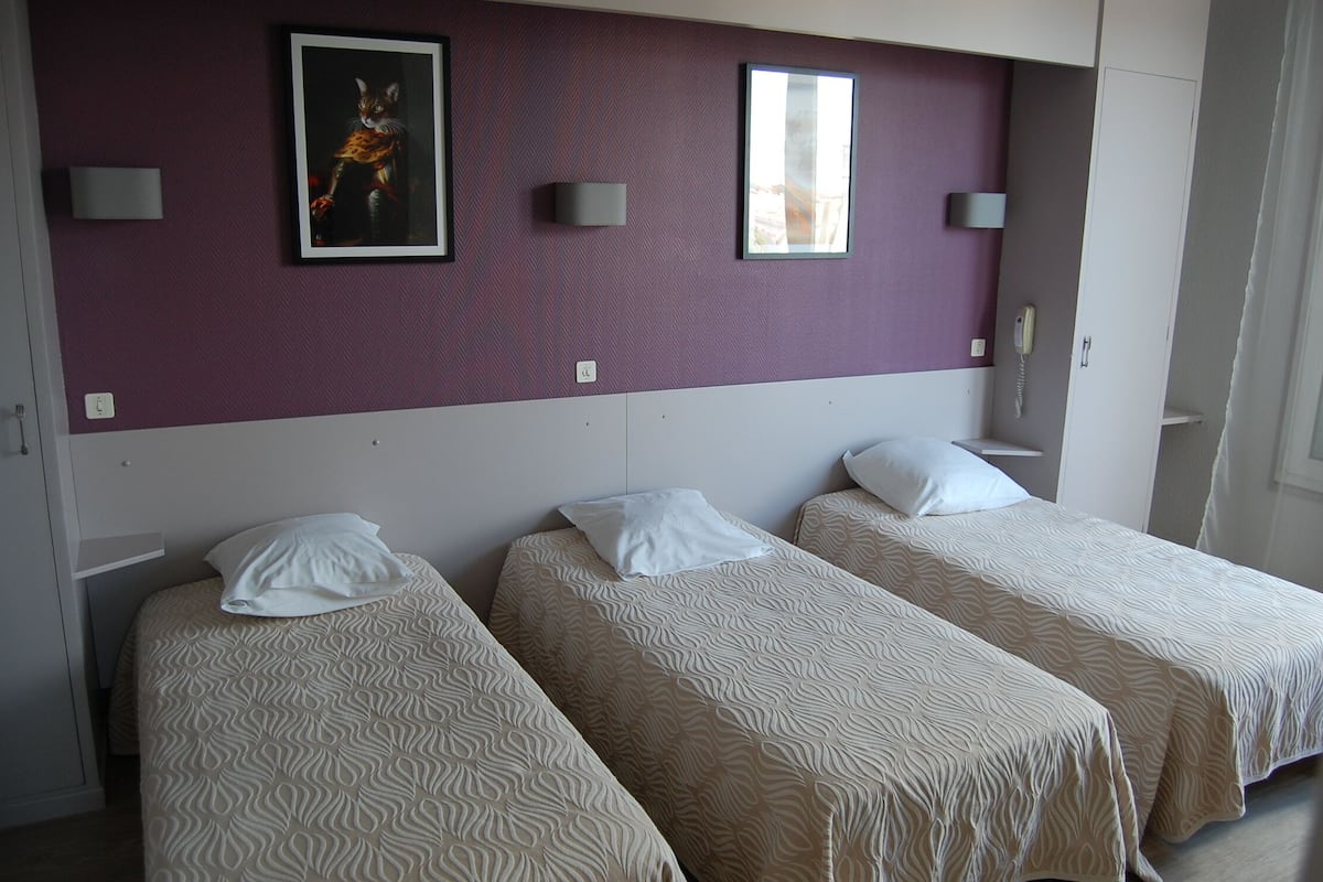A hotel room with two single beds, a purple wall, and a framed picture.