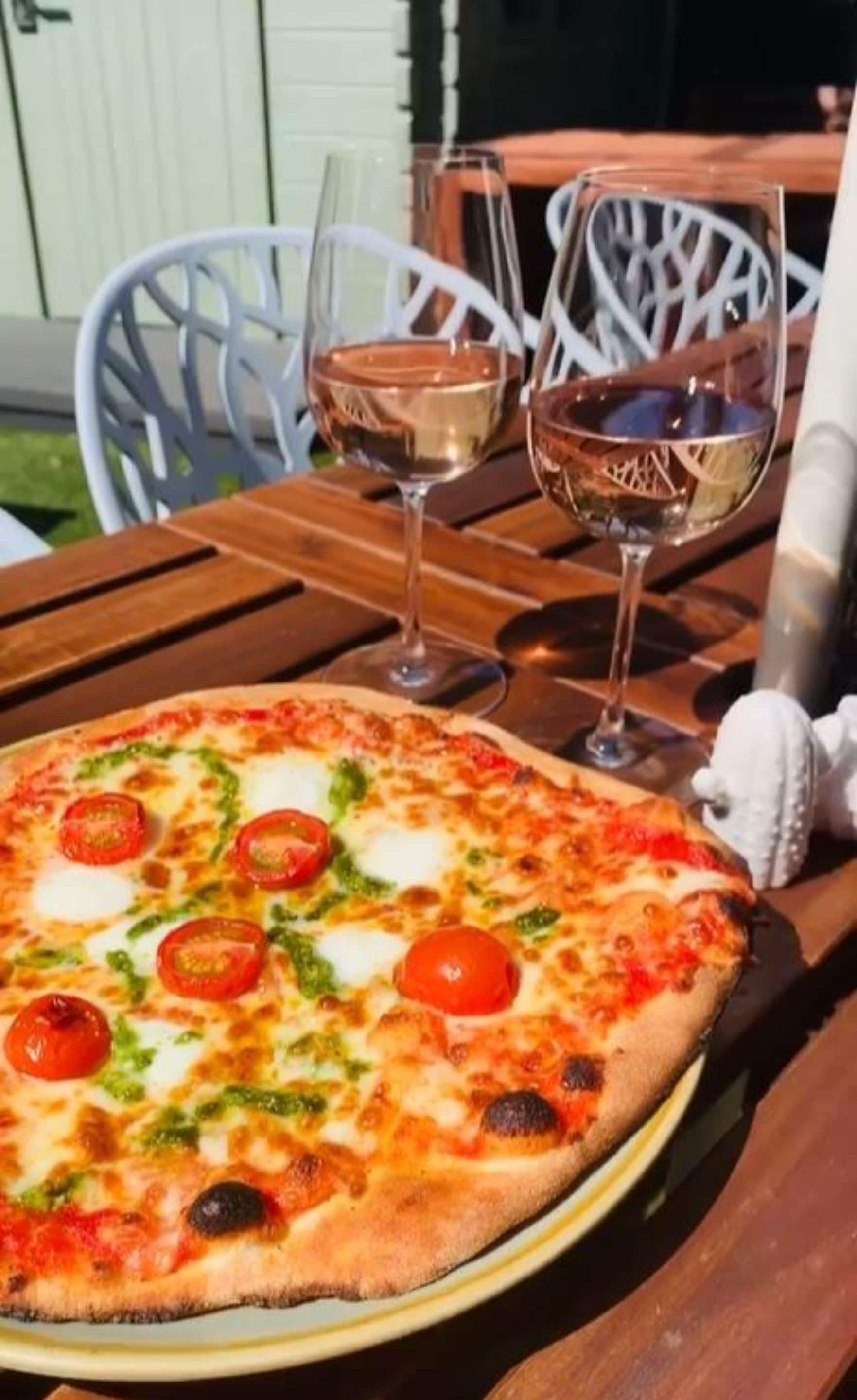 A pizza on a wooden table with two glasses of white wine.