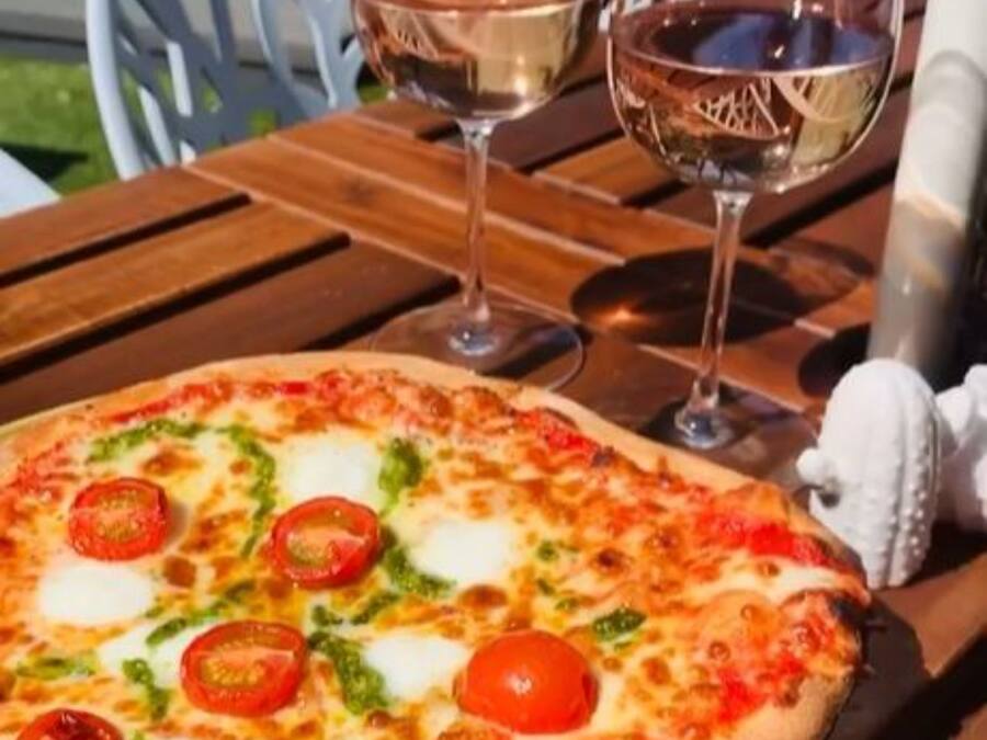 A pizza on a wooden table with two glasses of white wine.