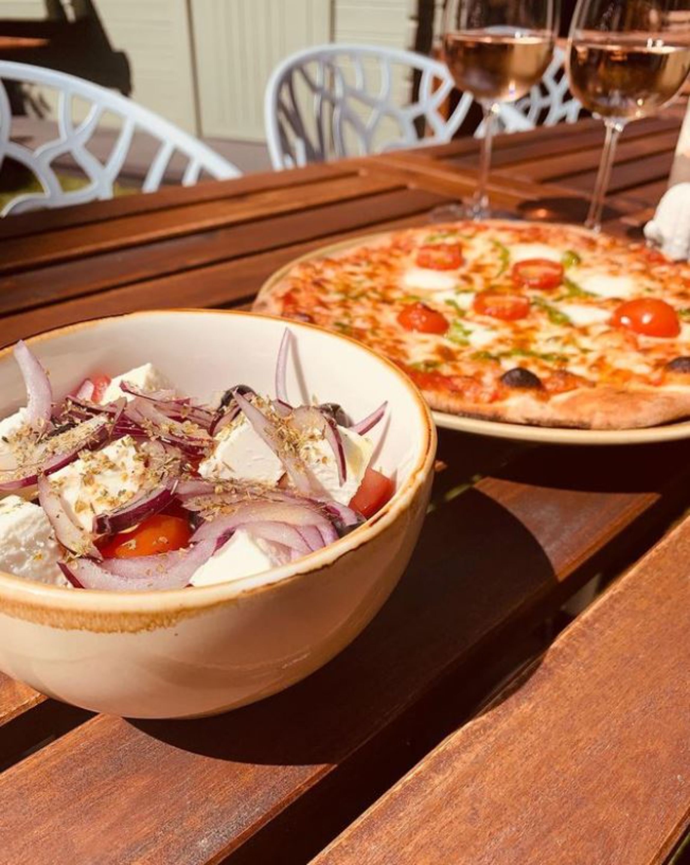 Una mesa de madera con un tazón de ensalada y una pizza.