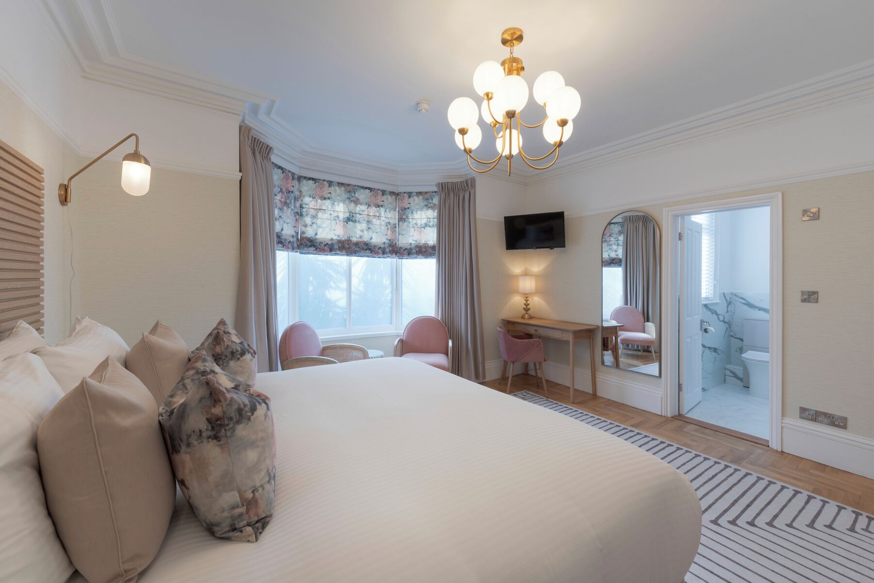 Habitación de hotel con una cama grande, un escritorio con silla, un televisor y un baño visible a través de una puerta abierta.
