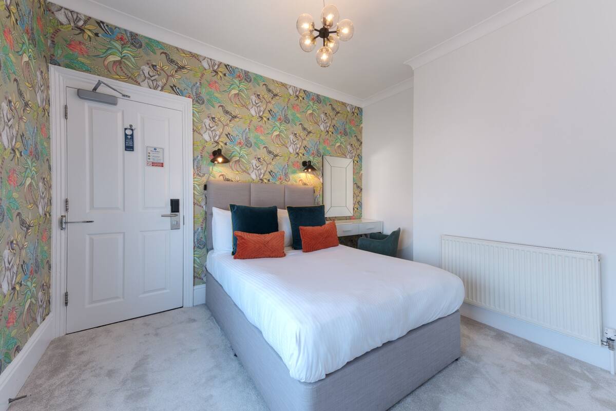 Un dormitorio con cama, cómoda, espejo y pared con estampado floral.