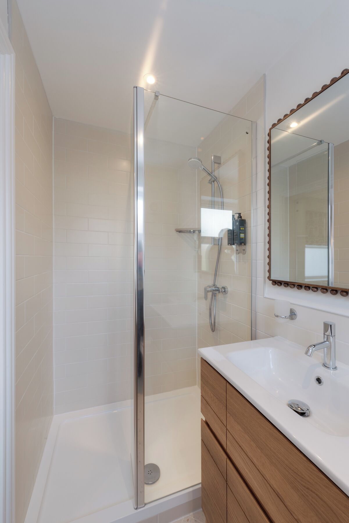A modern bathroom with a glass shower enclosure, a white sink, and wooden cabinetry.
