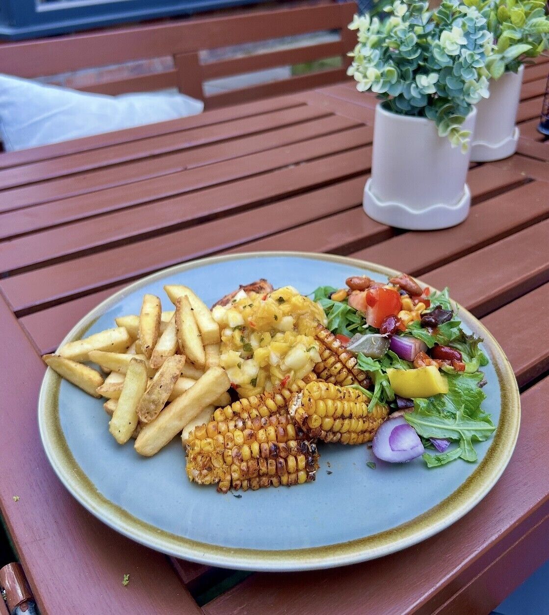Un plato con papas fritas, mazorca asada y una ensalada sobre una mesa de madera.