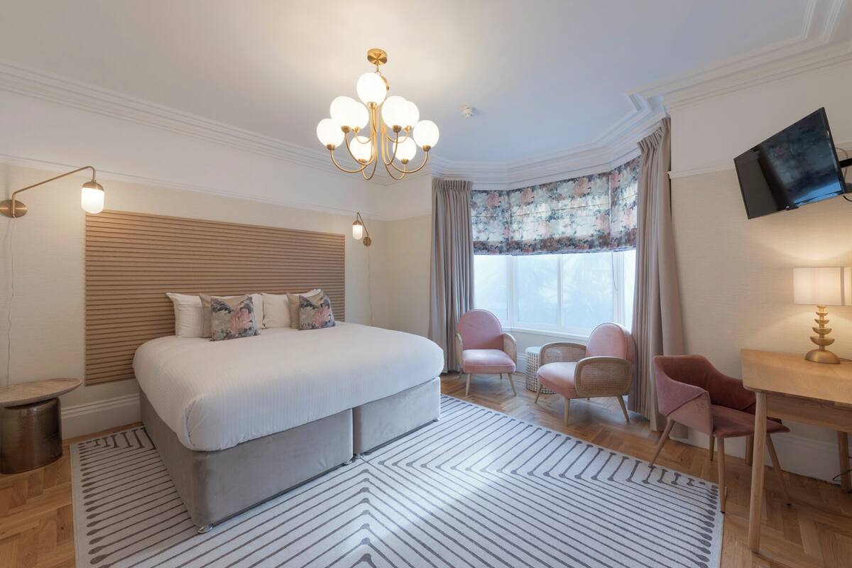 Una habitación de hotel con una cama grande, un escritorio, una silla, un televisor y una araña.